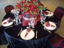 Round table dressed with black linen, place settings and a centre piece of red roses